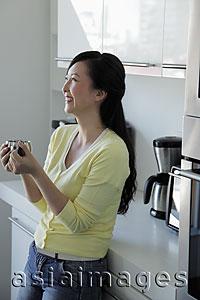 Asia Images Group - Woman leaning against kitchen counter holding coffee mug