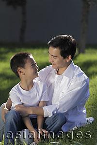 Asia Images Group - Father and son sitting on grass smiling at eachother