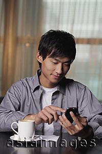 Asia Images Group - Young man sitting at a table texting on phone