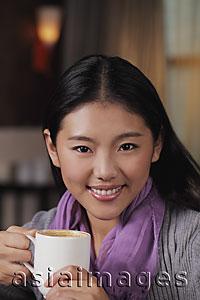 Asia Images Group - Head shot of young woman holding coffee cup and smiling
