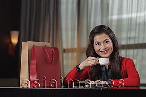 Asia Images Group - Young woman sitting in restaurant with shopping bags holding cup