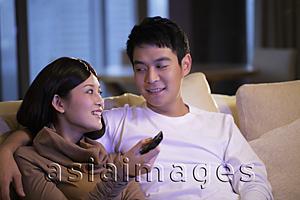 Asia Images Group - Young couple sitting on sofa watching TV together