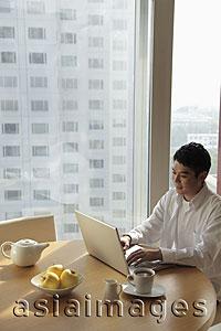 Asia Images Group - Young man sitting at a table working on laptop computer