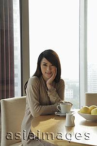 Asia Images Group - Young woman sitting at a table smiling