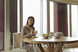 Asia Images Group - Young woman sitting at a table drinking tea