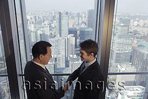 Asia Images Group - Two men shaking hands in front of a window with a view of the city of Beijing
