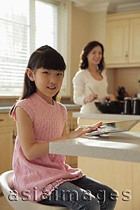 Asia Images Group - Mother watching her young daughter play on a digital tablet as she cooks
