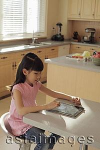 Asia Images Group - Young girl plays on a digital tablet computer in the kitchen
