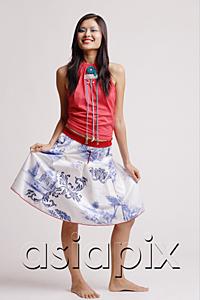 AsiaPix - Young woman, looking at camera, smiling, holding skirt