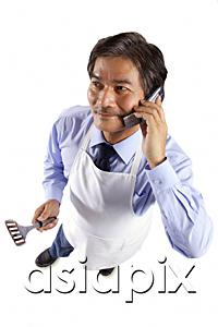 AsiaPix - Mature man wearing apron, holding spatula and using mobile phone