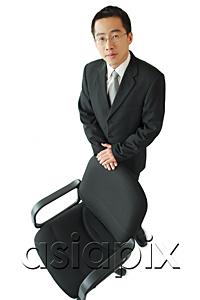AsiaPix - Businessman standing next to office chair, looking at camera