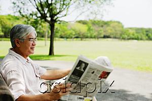 AsiaPix - Senior man sitting in park reading newspaper