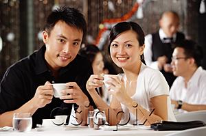 AsiaPix - Couple in restaurant, holding cups, smiling at camera