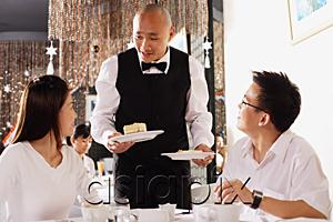 AsiaPix - Couple in restaurant, waiter standing, holding plates of dessert