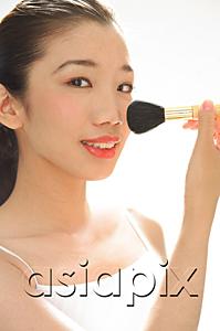AsiaPix - Woman holding make-up brush to face, looking at camera