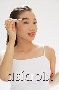 AsiaPix - Woman holding brush to eyebrows, looking at camera