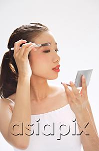 AsiaPix - Woman holding brush to eyebrows, looking at compact mirror