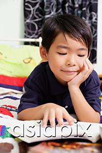 AsiaPix - Boy lying on bed, hand on chin, reading a book
