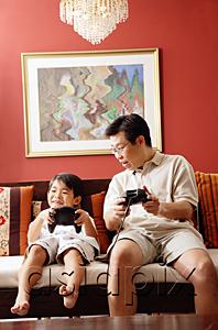 AsiaPix - Father and son sitting side by side on sofa, playing video game
