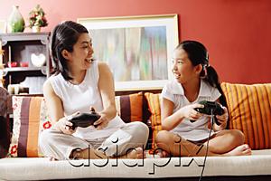 AsiaPix - Mother and daughter on sofa, holding video game controllers, looking at each other
