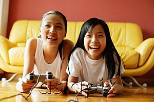 AsiaPix - Two sisters in living room, lying on floor playing video games
