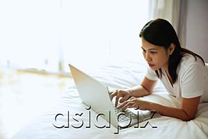 AsiaPix - Woman lying on bed, using laptop