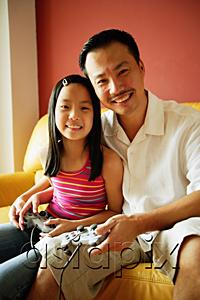 AsiaPix - Father and daughter looking at camera, holding video game controllers