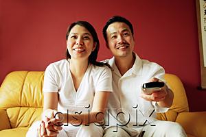 AsiaPix - Couple sitting on sofa, watching TV, man holding TV remote control