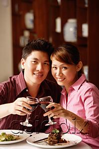 AsiaPix - Couple in restaurant, toasting with wine glasses, looking at camera