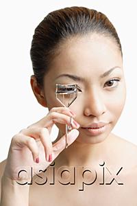 AsiaPix - Young woman holding eyelash curler, looking at camera