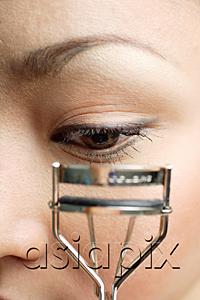 AsiaPix - Young woman holding eyelash curler near eye, close up