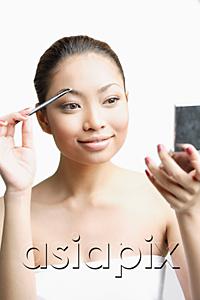 AsiaPix - Young woman using eyebrow brush, looking at compact
