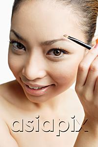 AsiaPix - Young woman using eyebrow brush, looking at camera
