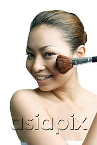 AsiaPix - Woman applying blusher with make-up brush, smiling at camera