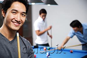 AsiaPix - Man holding pool cue, smiling at camera, people in the background