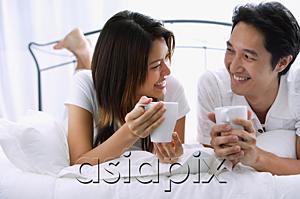 AsiaPix - Couple on bed, holding mugs, smiling at each other
