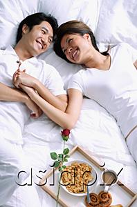 AsiaPix - Couple lying on bed, holding hands, breakfast on tray next to them