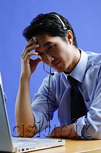 AsiaPix - Man wearing headset, using laptop, hand on head