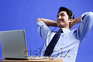 AsiaPix - Man wearing headset, using laptop, leaning back, hands behind head