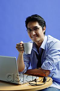 AsiaPix - Man sitting in front of laptop, holding mug, smiling at camera