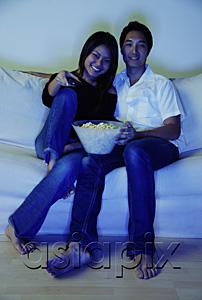 AsiaPix - Couple sitting on sofa, watching TV, bowl of popcorn between them