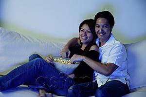 AsiaPix - Couple sitting on sofa, watching TV, eating popcorn