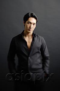 AsiaPix - Man dressed in black, standing against black background, hands in pocket