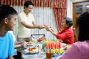 AsiaPix - Adult son passing plate of food to senior woman