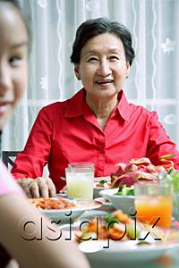 AsiaPix - Senior adult at dining table, smiling at camera, granddaughter in the foreground