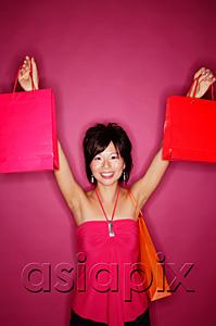 AsiaPix - Young woman against pink background holding up shopping bags