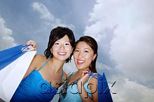 AsiaPix - Two women standing cheek to cheek, carrying shopping bags, low angle view