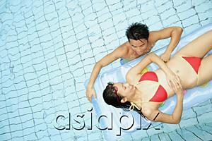 AsiaPix - Couple in swimming pool, woman lying on pool raft, man next to her