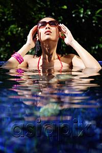 AsiaPix - Woman sitting in swimming pool, touching sunglasses