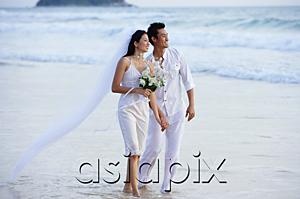 AsiaPix - Bride and groom walking on beach, holding hands, looking away